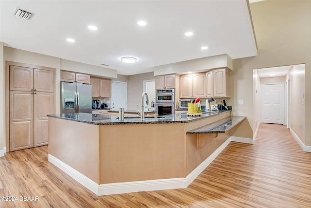 kitchen with sink, kitchen peninsula, appliances with stainless steel finishes, dark stone countertops, and light hardwood / wood-style flooring