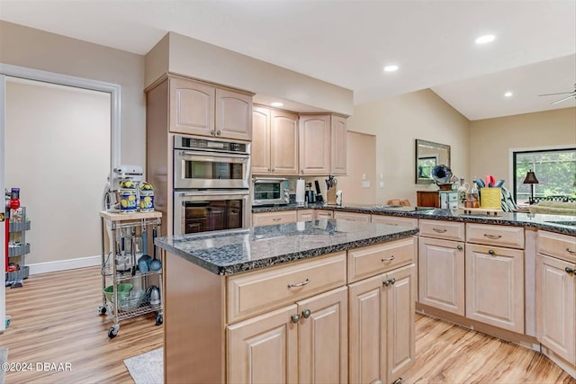 kitchen featuring dark stone counters, vaulted ceiling, double oven, light brown cabinets, and light hardwood / wood-style flooring