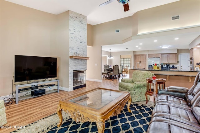 living room with a towering ceiling, a stone fireplace, light wood-type flooring, sink, and ceiling fan