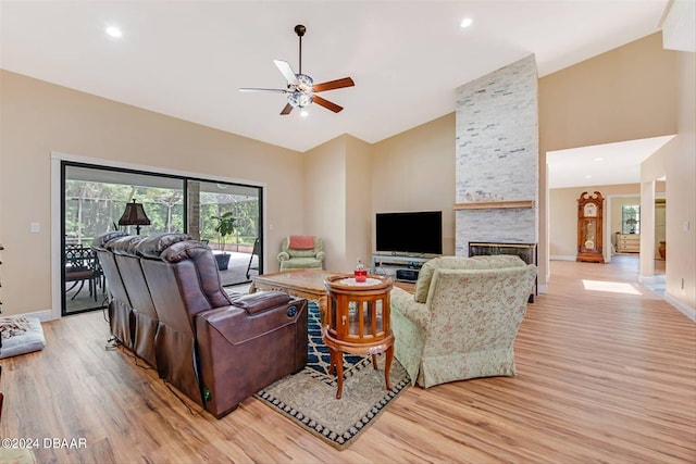 living room with high vaulted ceiling, light wood-type flooring, a stone fireplace, and ceiling fan