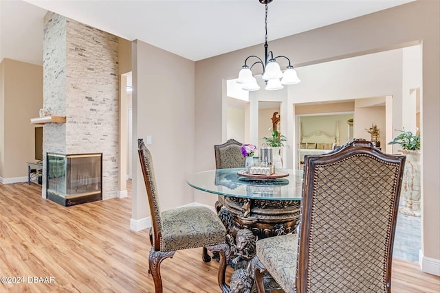 dining room featuring a stone fireplace, light wood-type flooring, and a notable chandelier