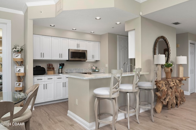 kitchen featuring light stone counters, ornamental molding, light wood-type flooring, a breakfast bar, and white cabinets