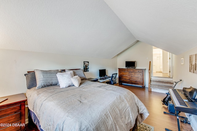 bedroom with lofted ceiling, hardwood / wood-style floors, and a textured ceiling