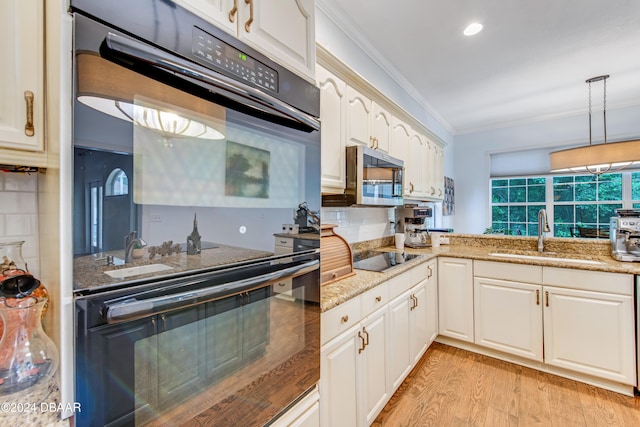 kitchen with black appliances, ornamental molding, hanging light fixtures, sink, and light hardwood / wood-style flooring