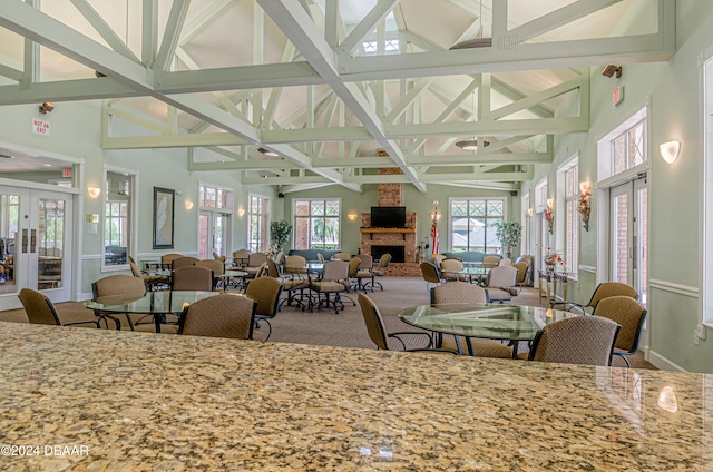 carpeted dining space with a fireplace, high vaulted ceiling, and french doors