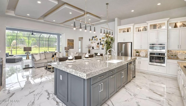 kitchen with stainless steel appliances, a center island with sink, gray cabinets, light stone countertops, and white cabinetry