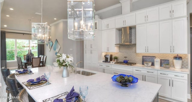 kitchen featuring stainless steel gas stovetop, sink, ornamental molding, wall chimney range hood, and white cabinetry