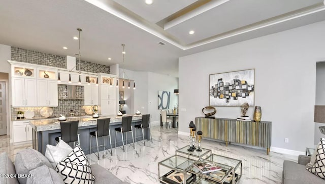 kitchen with a center island with sink, a breakfast bar, hanging light fixtures, white cabinets, and decorative backsplash