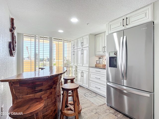 kitchen with white cabinetry, stainless steel fridge, light hardwood / wood-style floors, and a textured ceiling