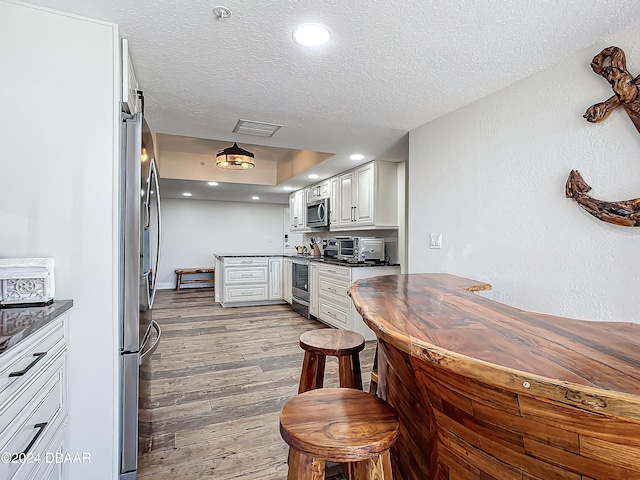 kitchen with a textured ceiling, light wood-type flooring, stainless steel appliances, and white cabinetry