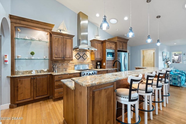 kitchen with a spacious island, stainless steel appliances, decorative light fixtures, and wall chimney range hood