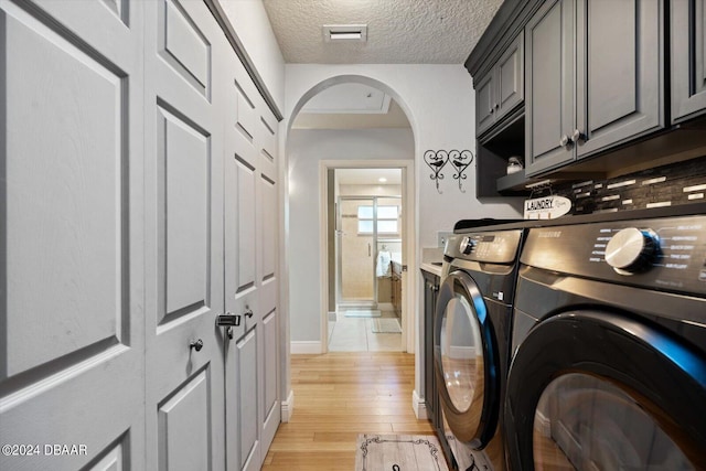 washroom featuring cabinets, light hardwood / wood-style floors, separate washer and dryer, and a textured ceiling