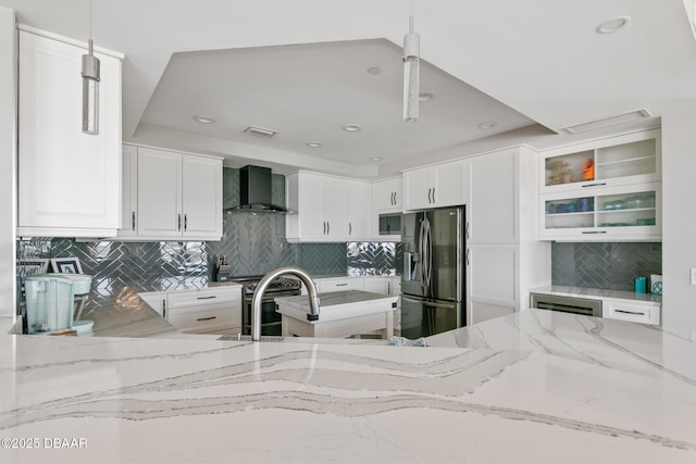 kitchen with tasteful backsplash, light stone counters, wall chimney exhaust hood, stainless steel appliances, and pendant lighting