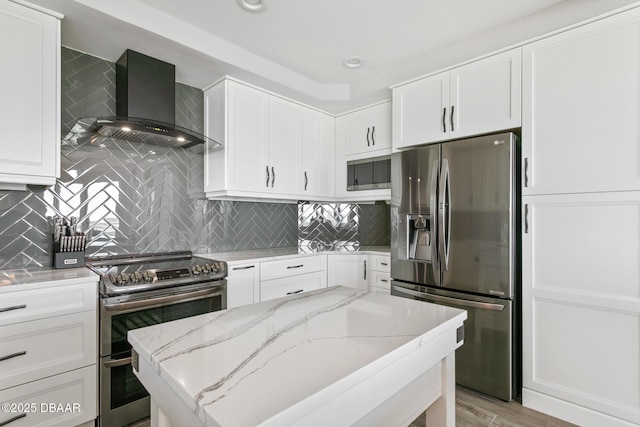 kitchen featuring appliances with stainless steel finishes, white cabinetry, light stone counters, and wall chimney range hood