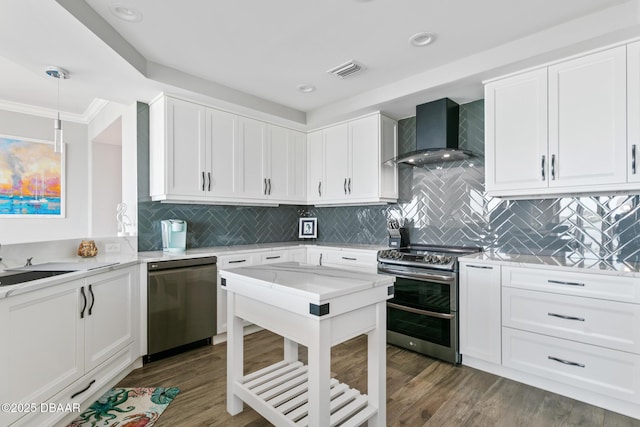 kitchen with wall chimney exhaust hood, white cabinetry, stainless steel appliances, and hanging light fixtures