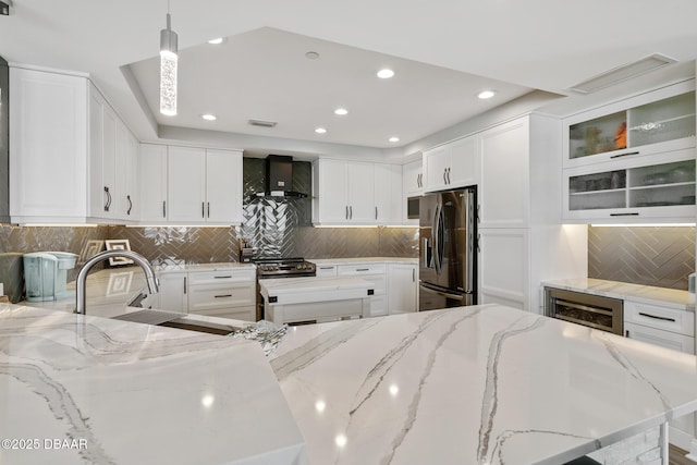 kitchen with light stone countertops, tasteful backsplash, stainless steel appliances, wall chimney range hood, and hanging light fixtures