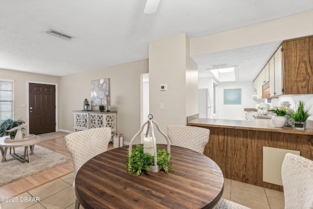 dining room featuring light tile patterned flooring, visible vents, a textured ceiling, and baseboards