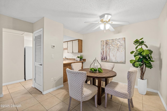dining space with baseboards, a ceiling fan, a textured ceiling, and light tile patterned flooring