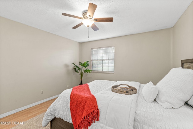 bedroom featuring a ceiling fan, a textured ceiling, wood finished floors, and baseboards