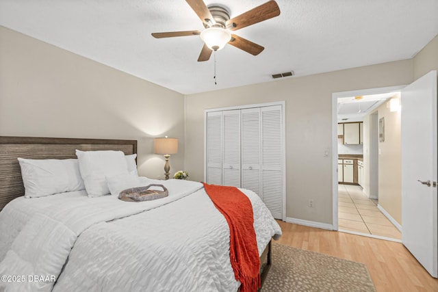 bedroom featuring a closet, light wood finished floors, baseboards, visible vents, and a ceiling fan