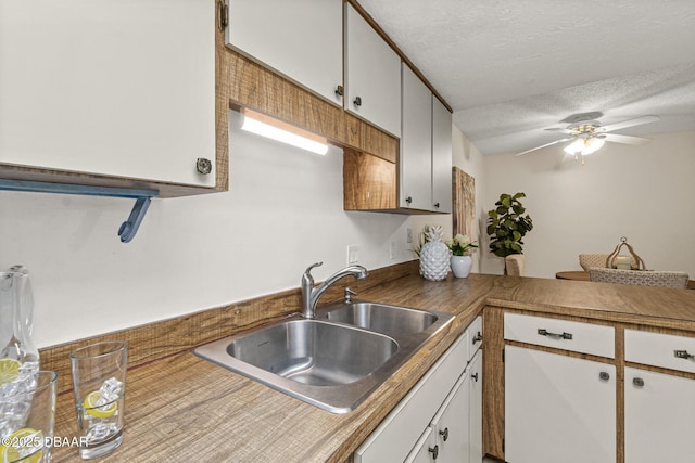 kitchen with a textured ceiling, a sink, ceiling fan, and white cabinetry