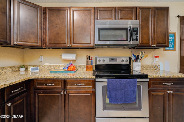 kitchen with light stone counters, appliances with stainless steel finishes, and dark brown cabinetry