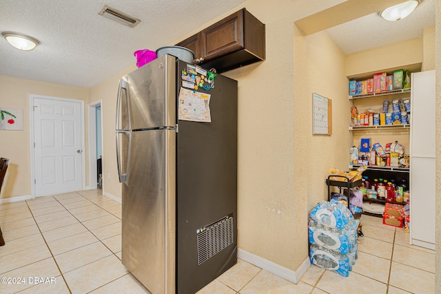 kitchen with dark brown cabinetry, a textured ceiling, stainless steel refrigerator, and light tile patterned flooring