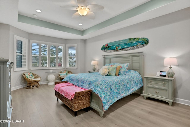 bedroom with light wood-type flooring, a tray ceiling, and ceiling fan