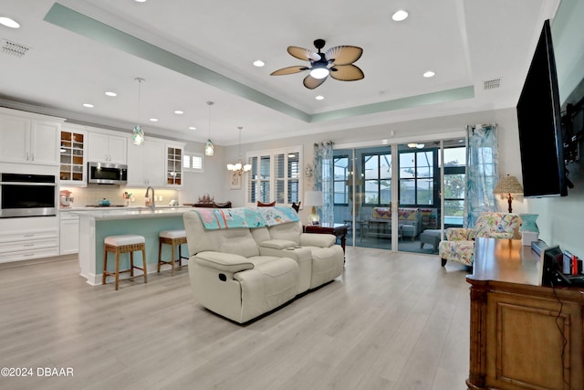 living room with light hardwood / wood-style floors, ceiling fan with notable chandelier, a raised ceiling, and sink