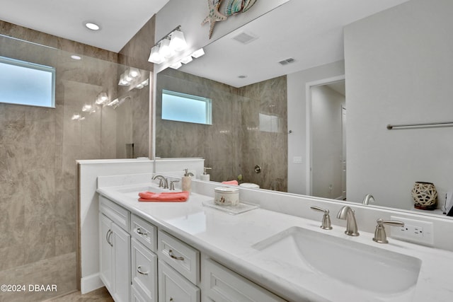 bathroom with tiled shower, vanity, and a healthy amount of sunlight