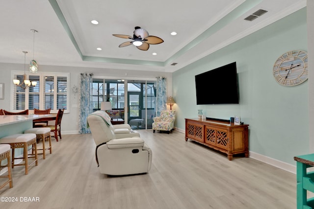 living room with ceiling fan with notable chandelier, a raised ceiling, crown molding, and light hardwood / wood-style flooring