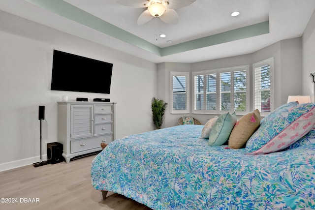 bedroom with ceiling fan, light hardwood / wood-style flooring, and a tray ceiling