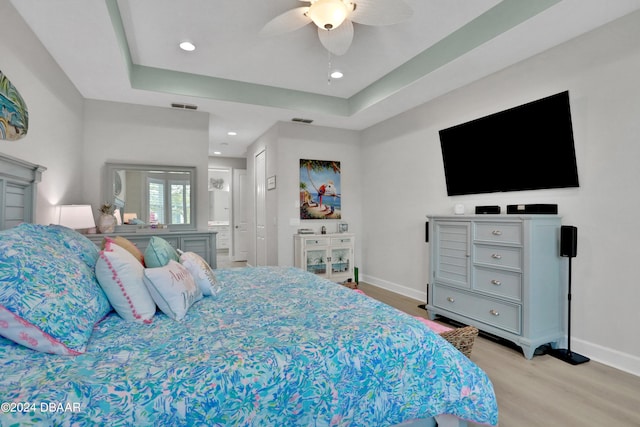 bedroom with light wood-type flooring, ceiling fan, and a tray ceiling