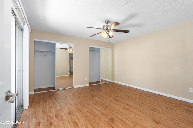 unfurnished bedroom featuring ceiling fan, light wood-type flooring, a textured ceiling, and two closets