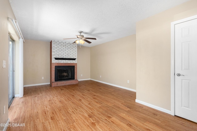 unfurnished living room with ceiling fan, a brick fireplace, a textured ceiling, and light wood-type flooring