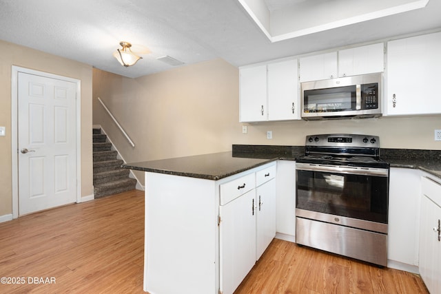 kitchen featuring white cabinetry, light hardwood / wood-style flooring, dark stone countertops, kitchen peninsula, and stainless steel appliances