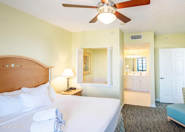 bedroom featuring ensuite bath, visible vents, a textured ceiling, and ceiling fan