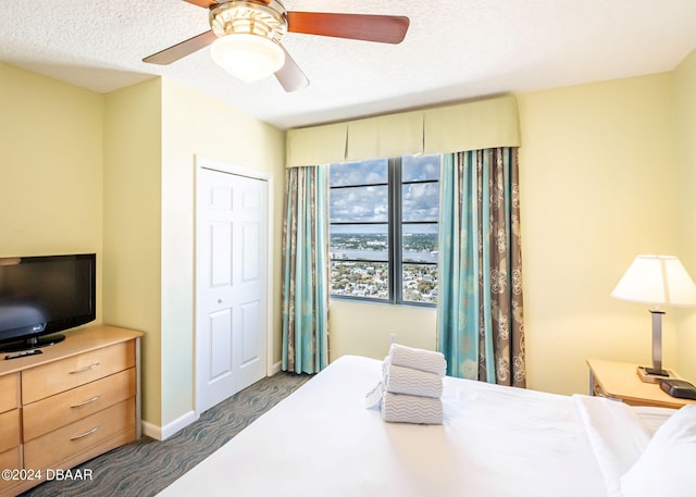 bedroom with baseboards, dark carpet, a closet, a textured ceiling, and a ceiling fan