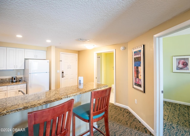 kitchen featuring a breakfast bar, light stone counters, dark carpet, white cabinetry, and freestanding refrigerator