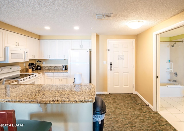 kitchen featuring visible vents, a breakfast bar, white cabinetry, white appliances, and light stone countertops