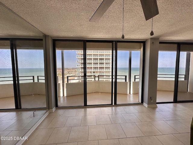 interior space with floor to ceiling windows, a water view, a ceiling fan, a textured ceiling, and baseboards