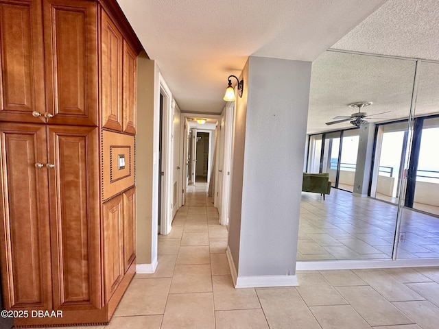 corridor featuring a textured ceiling, baseboards, and light tile patterned floors