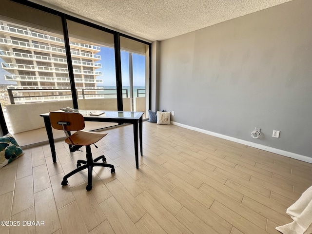 office with a textured ceiling, expansive windows, baseboards, and wood finished floors