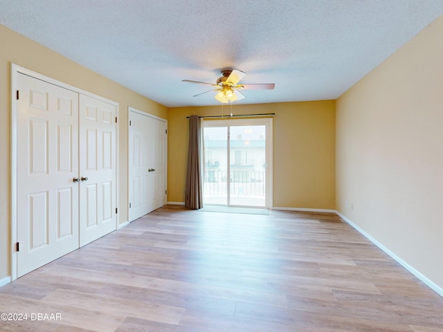 unfurnished bedroom with light wood-type flooring, a textured ceiling, baseboards, and multiple closets