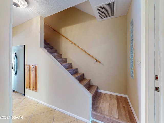 stairs featuring visible vents, a textured ceiling, baseboards, and tile patterned floors