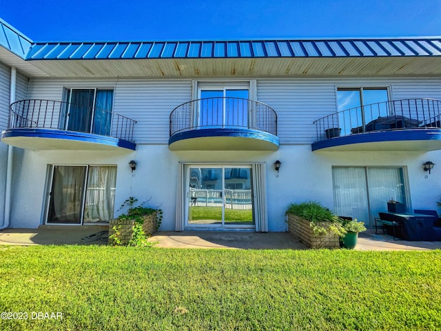 rear view of property featuring a yard, a balcony, and stucco siding