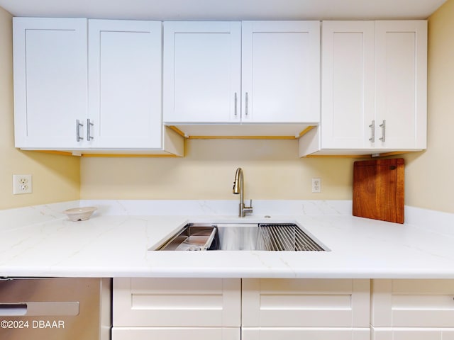 kitchen with light stone counters, a sink, and white cabinets