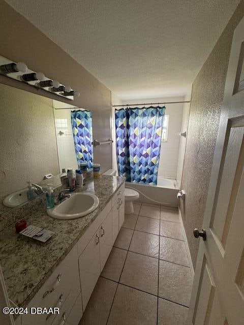 full bathroom featuring vanity, toilet, a textured ceiling, tile patterned flooring, and shower / tub combo with curtain