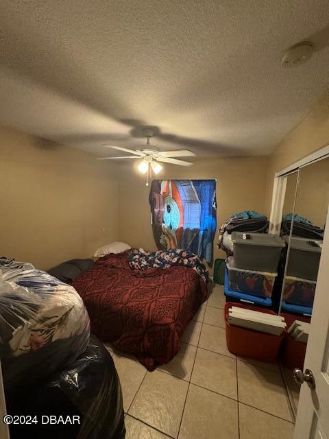 bedroom with ceiling fan, a textured ceiling, light tile patterned floors, and a closet