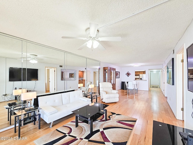 living room featuring light hardwood / wood-style flooring, a textured ceiling, and ceiling fan